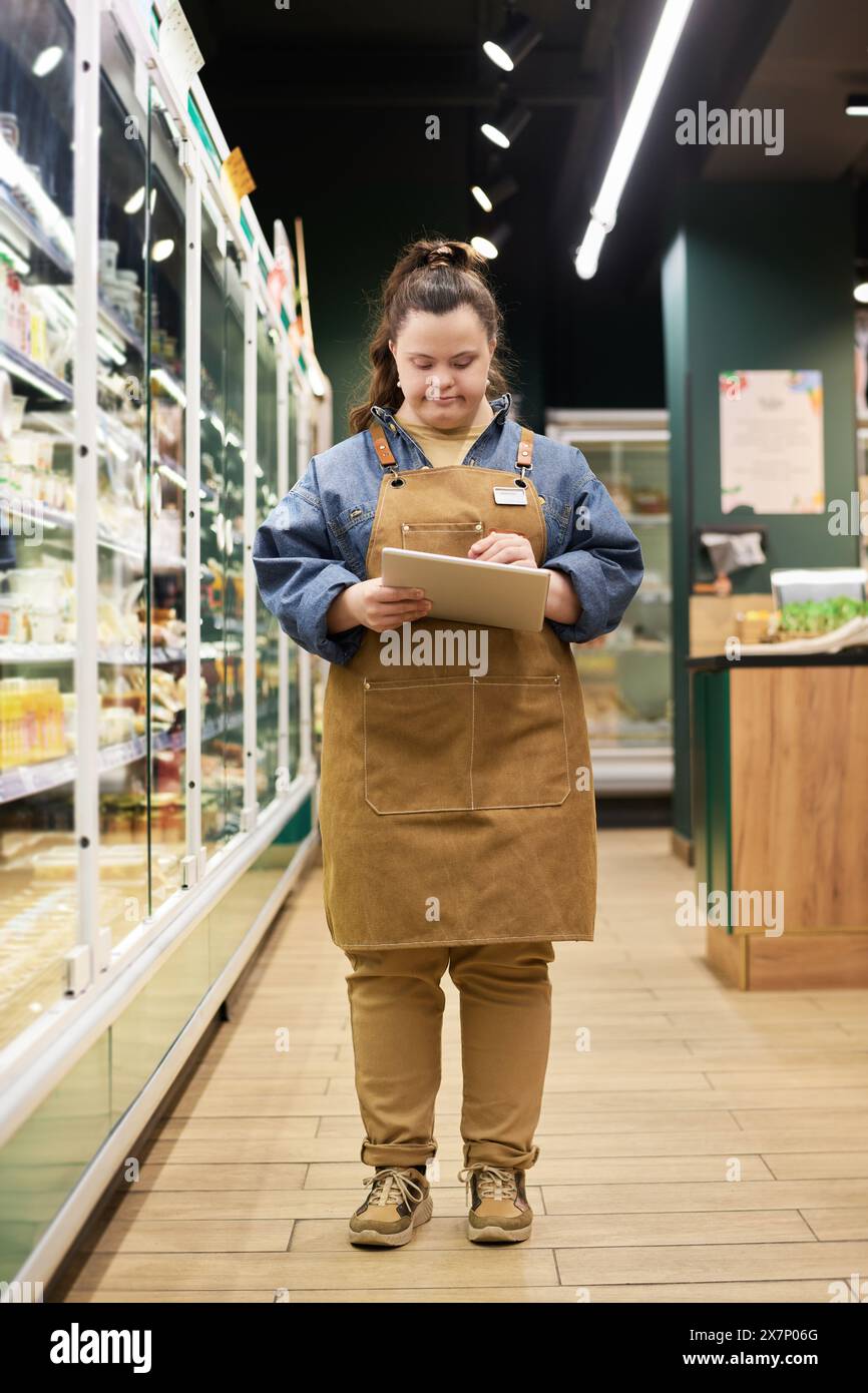 Vertikales Vollbildnis einer behinderten jungen Frau, die im Supermarkt arbeitet und mit einem Tablet in Richtung Kamera läuft Stockfoto