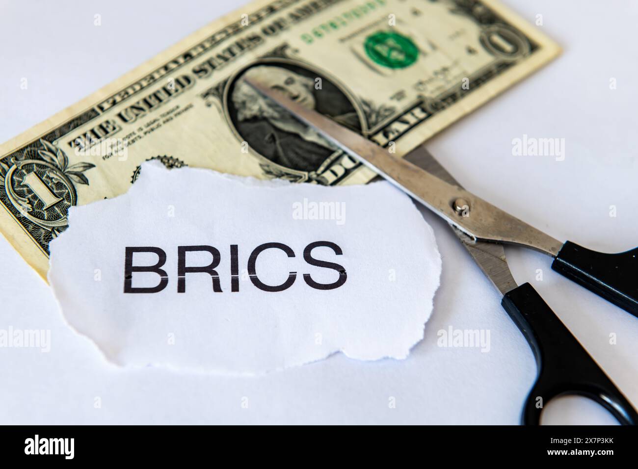 Ein Dollarisierungskonzept mit einer Dollarnote, dem Wort BRICS und einer weißen Schere. Stockfoto