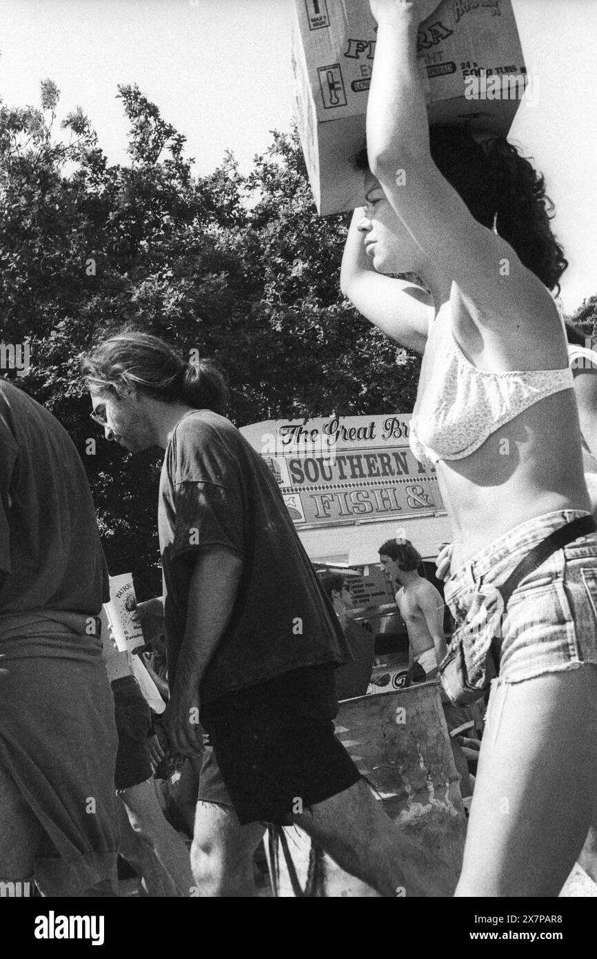 FOOD AREA, CROWD, HEATWAVE, NME STAGE, GLASTONBURY 95: eine Frau in Bikinioberteil und Jeans-Shorts trägt eine Box auf dem Kopf durch die Verkaufsstände in der extremen Hitze des Sommers in der Nähe des zweiten NME Stage Fields und beim Glastonbury Festival, Pilton Farm, Somerset, England, 24. Juni 1995. 1995 feierte das Festival sein 25-jähriges Bestehen. Viele Menschen hatten an dem besonders heißen Wochenende Probleme mit dem Hitzschlag. Foto: ROB WATKINS Stockfoto