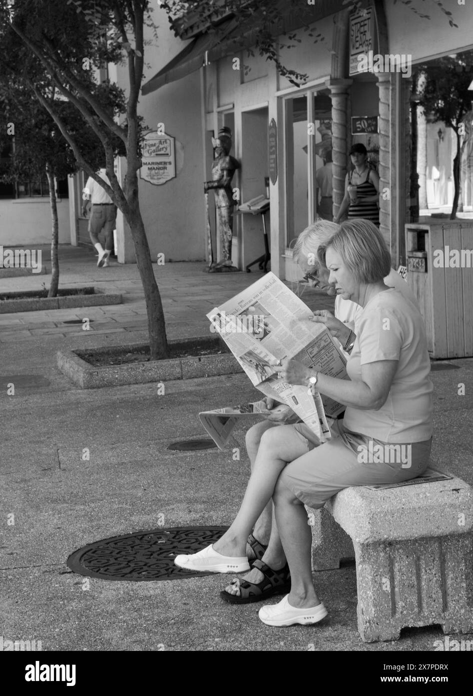 Ein Mann und eine Frau, die eine Zeitung lesen, während sie sich auf der St. George Street in St. Augustine, Florida, USA, ausruhen. Stockfoto