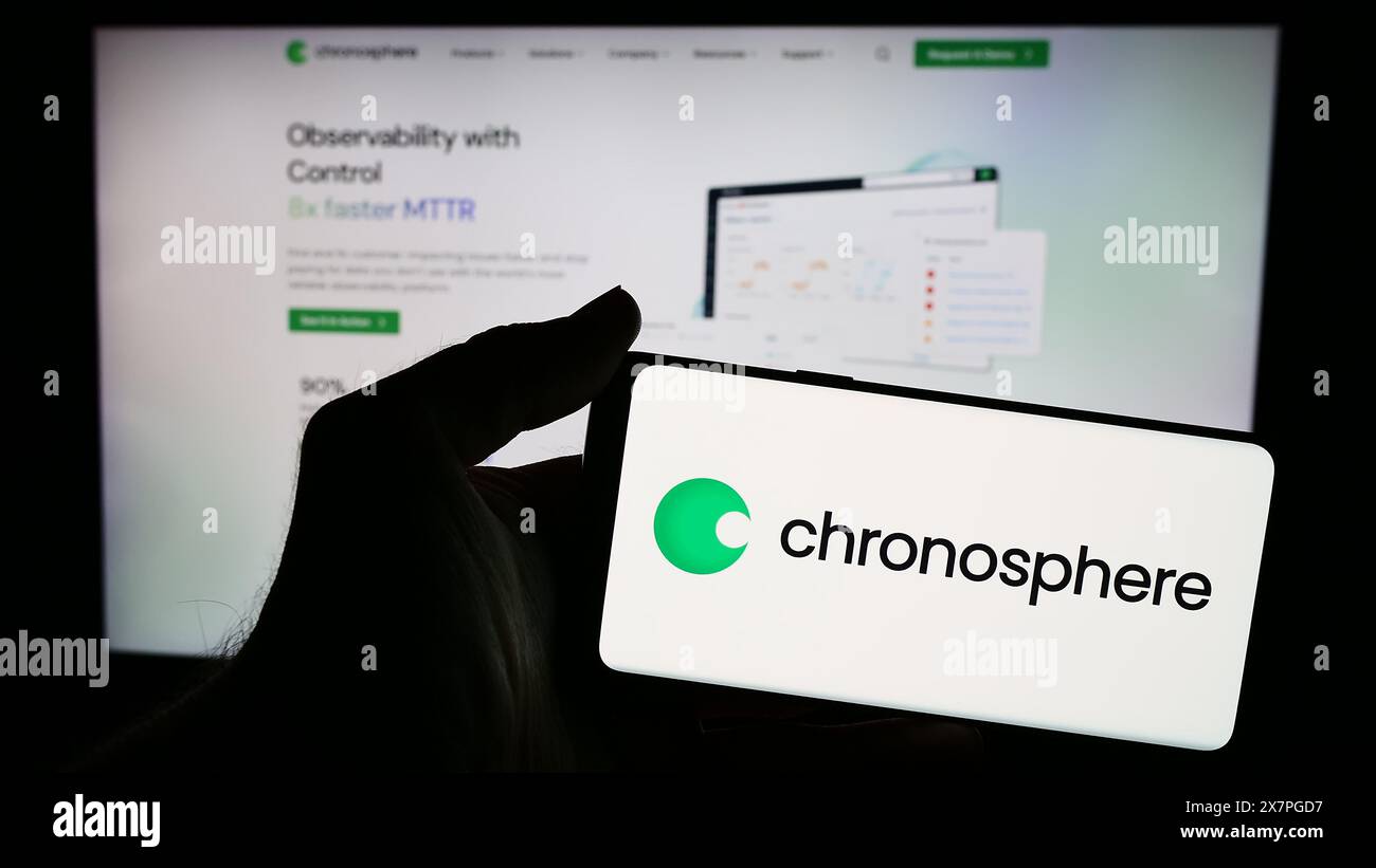 Person, die ein Mobiltelefon mit dem Logo der amerikanischen Beobachtungsplattform Chronosphere Inc. Vor der Webseite hält. Schwerpunkt auf dem Display des Telefons. Stockfoto