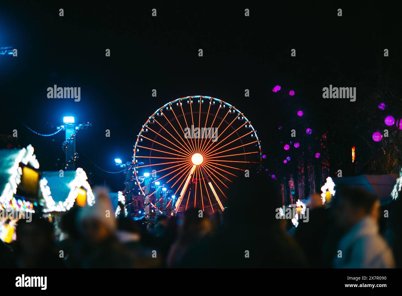 Ein pulsierendes Riesenrad erleuchtet die Nacht auf dem festlichen Weihnachtsmarkt in Brüssel, umgeben von Urlaubern und Dekorationen Stockfoto