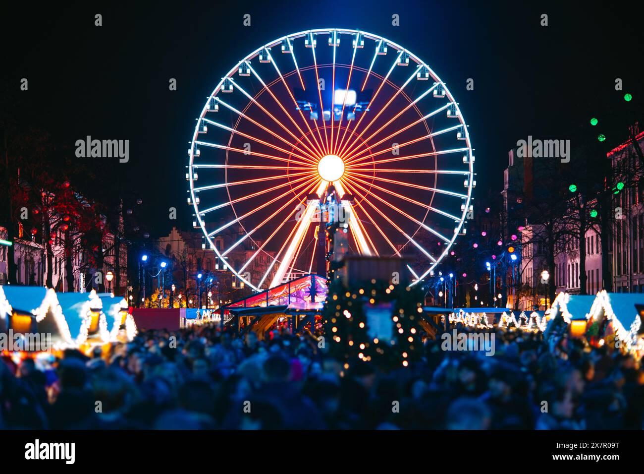 Ein bezaubernder Blick auf Brüssels geschäftigen Weihnachtsmarkt mit spektakulärem beleuchtetem Riesenrad und festlichen Menschenmassen Stockfoto