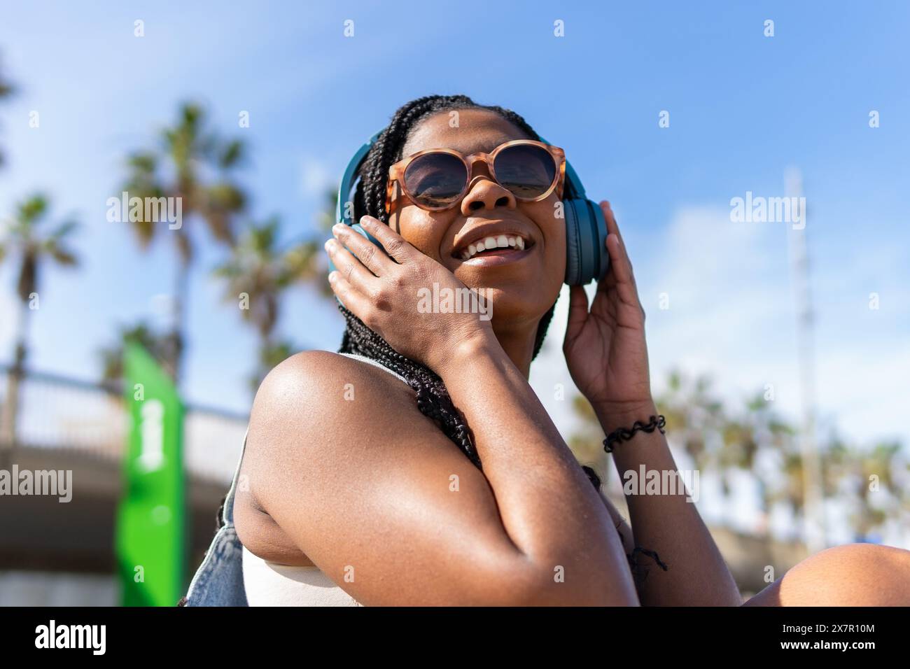 Frau genießt den Sommer in Barcelona, hört Musik mit Kopfhörern, mit Palmen und klarem Himmel im Hintergrund Stockfoto
