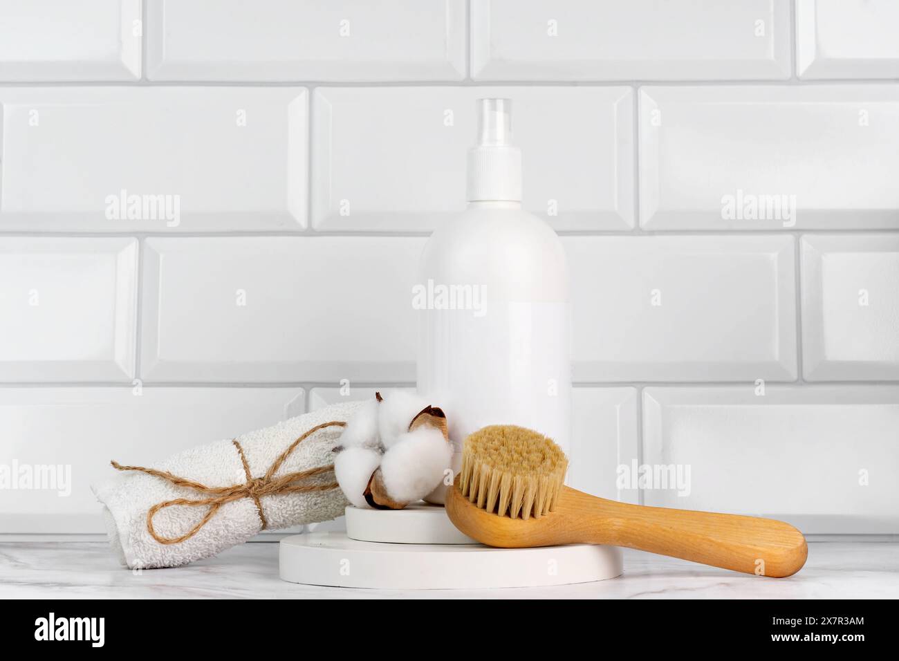 Ein sauberes, minimalistisches Arrangement besteht aus einer weißen Lotionsflasche, einer Naturfaserbürste, Baumwollknospen und einem Handtuch, das umweltfreundlich und nachhaltig ist Stockfoto