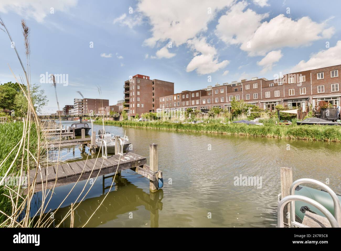 Ein ruhiger Blick auf einen ruhigen Wasserkanal, flankiert von modernen Wohngebäuden, private Boote an Holzstegen, üppiges Grün und klare blaue Ski Stockfoto