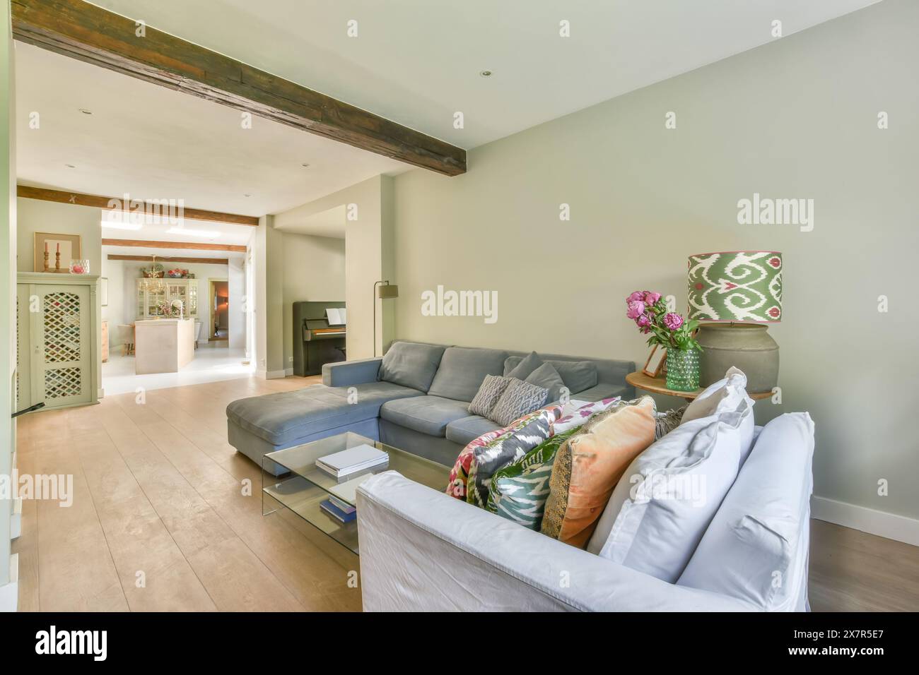 Ein wunderschön eingerichtetes Wohnzimmer mit freiliegenden Holzbalken, einem stilvollen grauen Sofa und floralen Akzenten machen den Raum zum Wohlfühlen Stockfoto