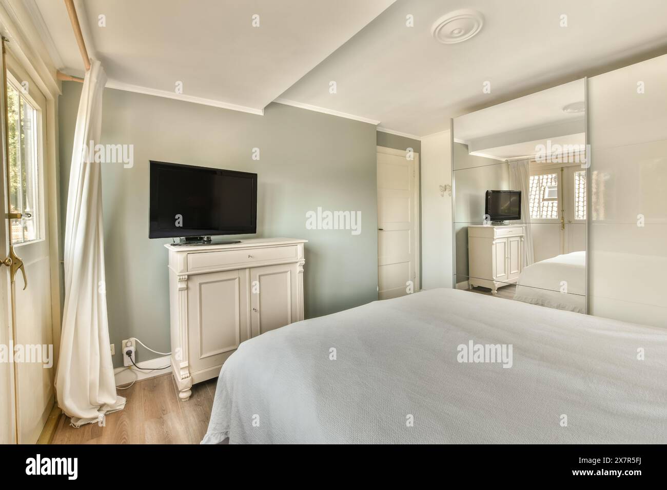 Modernes, aber einladendes Schlafzimmer mit großem Bett, Flachbildfernseher und Tageslicht Stockfoto