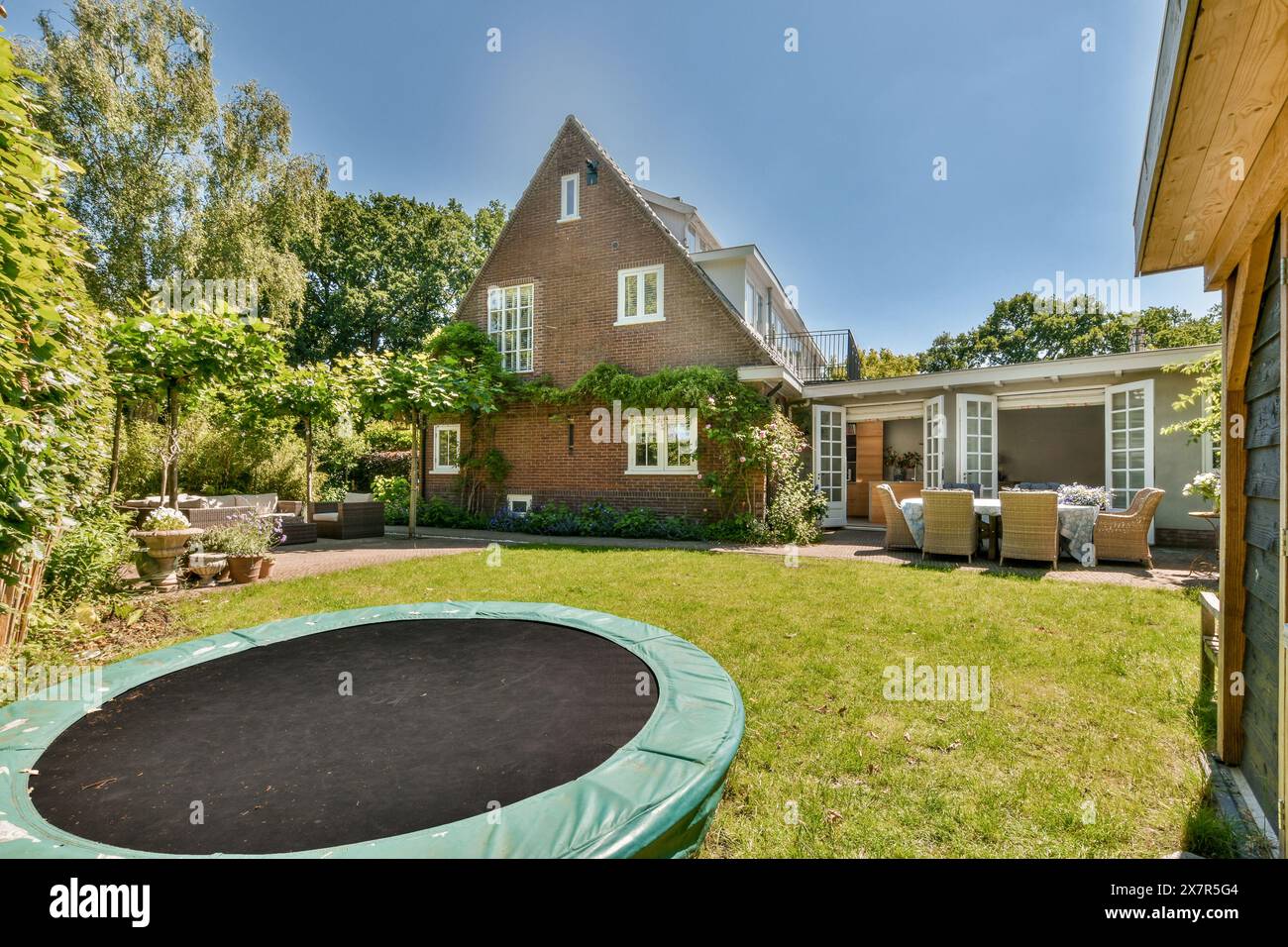 Eine ruhige Hinterhoflage eines Einfamilienhauses am Molenveenweg, mit üppigem Grün, einem Trampolin und einem gemütlichen Sitzbereich im Freien Stockfoto