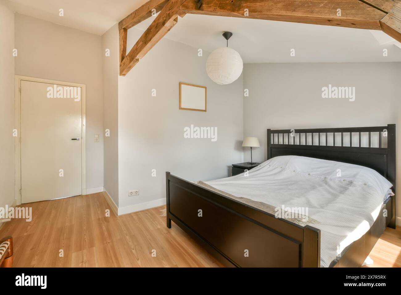 Ein gut beleuchtetes, minimalistisches Schlafzimmer mit Holzrahmen, freiliegenden Holzbalken und einfacher moderner Einrichtung. Stockfoto