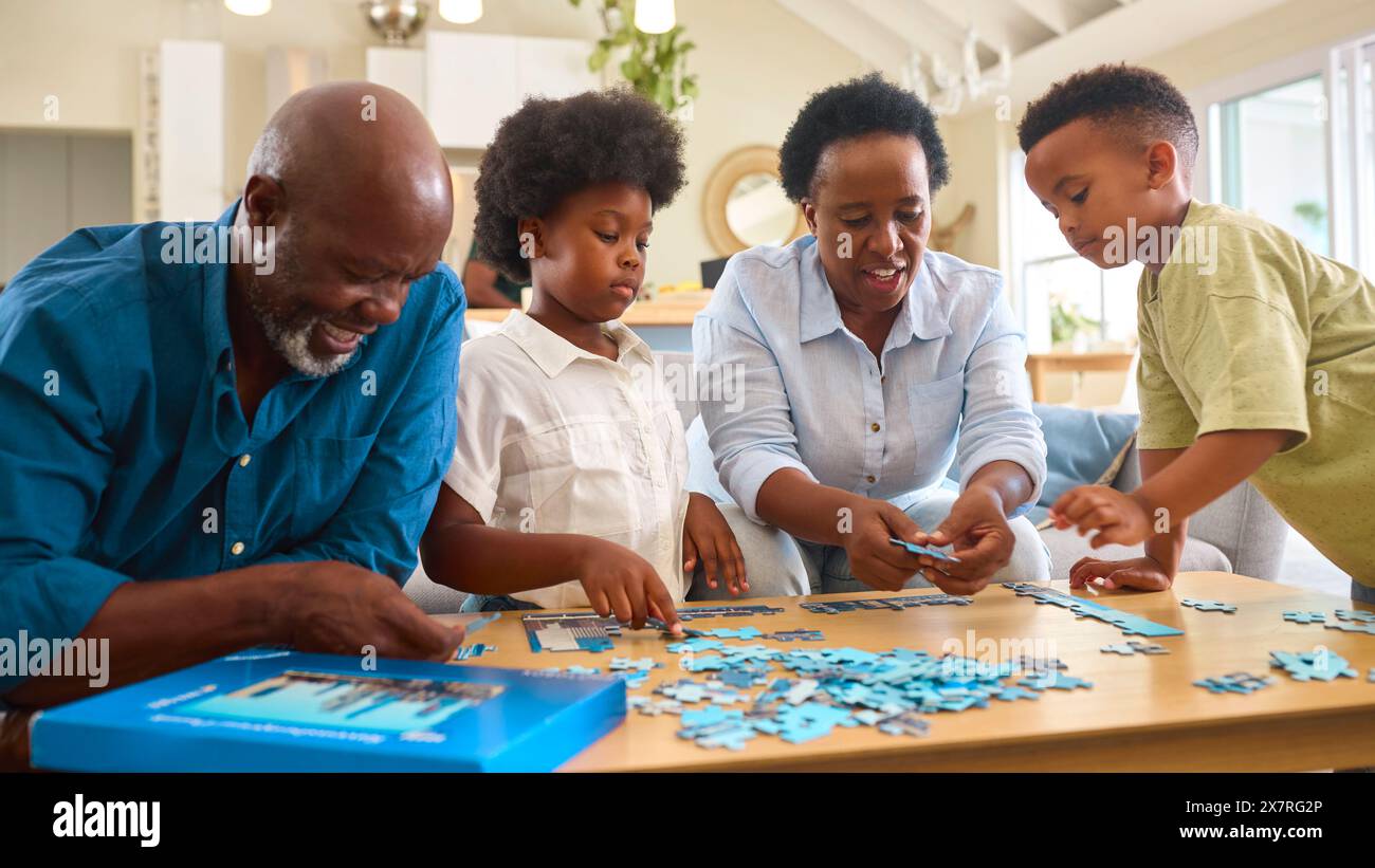 Großeltern Mit Enkelkindern Sitzen Zuhause Um Den Tisch Und Machen Gemeinsam Puzzle Stockfoto