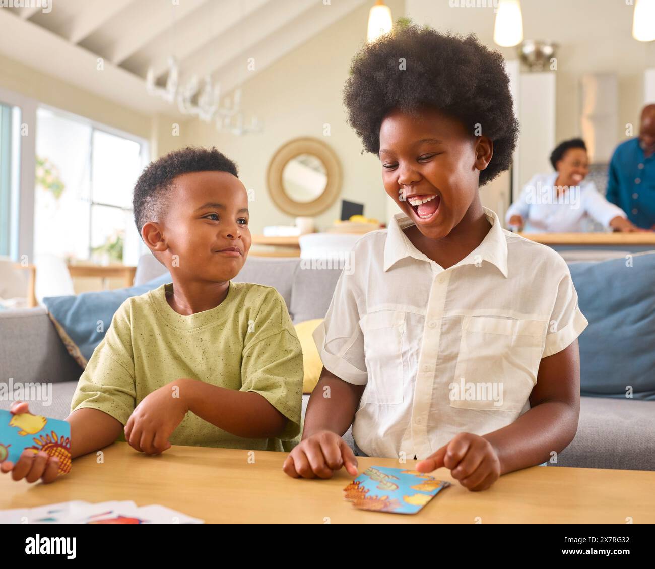 Junge Und Mädchen Spielen Zu Hause Kartenspiel Mit Multi-Generation-Familie Im Hintergrund Stockfoto