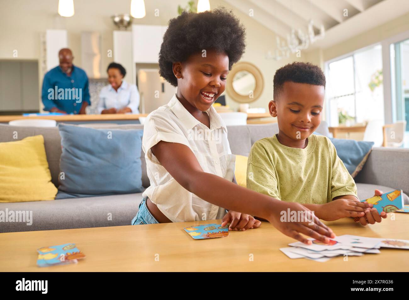 Junge Und Mädchen Spielen Zu Hause Kartenspiel Mit Multi-Generation-Familie Im Hintergrund Stockfoto