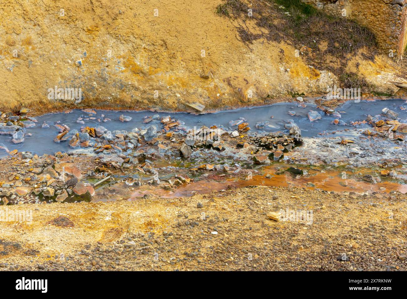 Blauer mineralischer Thermalfluss umgeben von orangefarbenem Schwefelboden und Steinen im Geothermalgebiet Seltun in Krysuvik, Island. Stockfoto