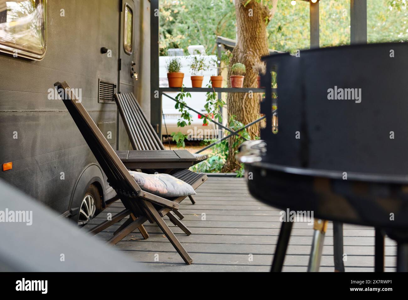 Terrasse mit einem Wohnmobil, Grill und Stühlen, ein romantischer Kurzurlaub in der Natur. Stockfoto