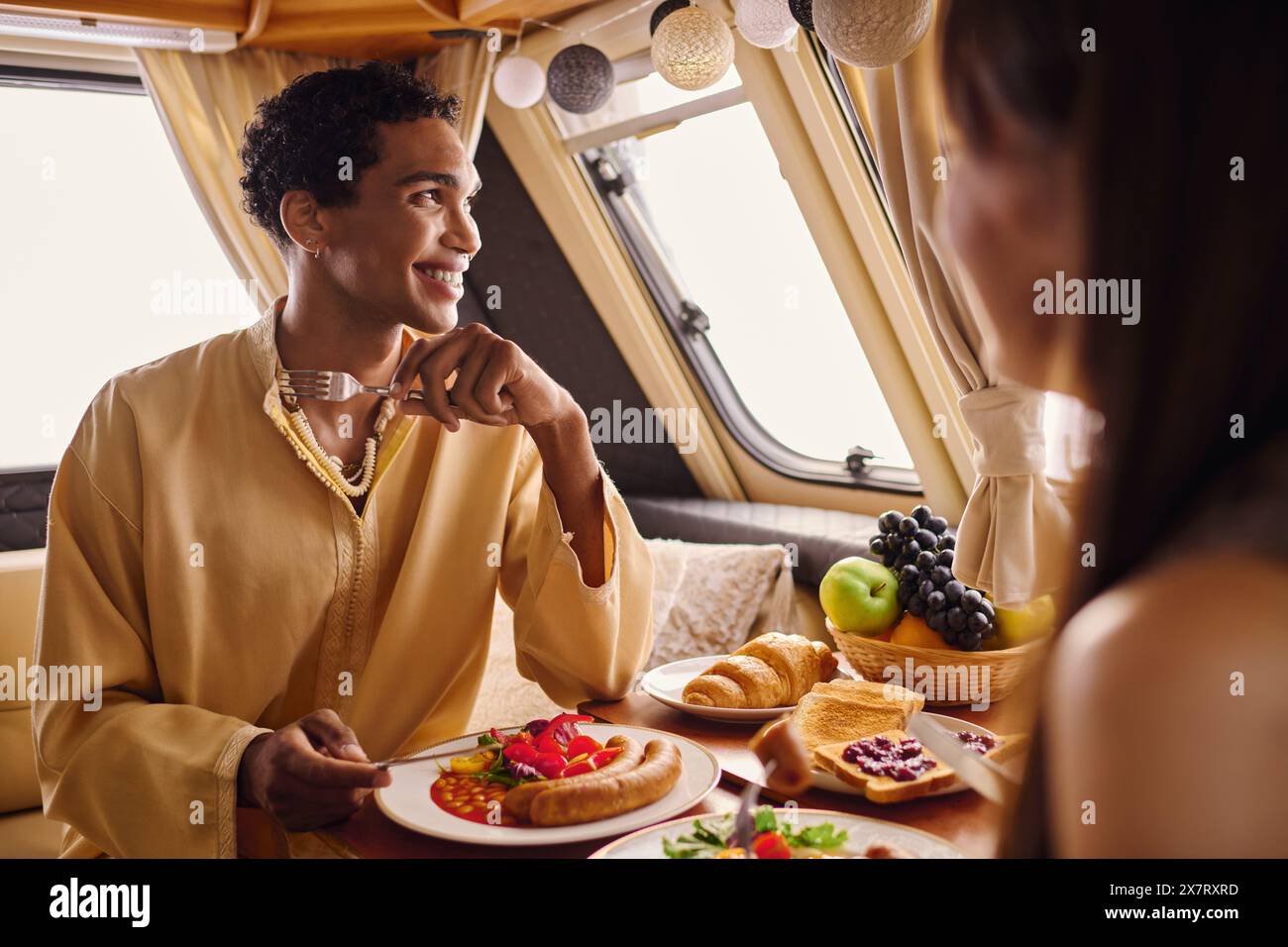 Ein interrassisches Paar, das ein köstliches Mittagessen in einem Wohnmobil genießt und ein romantisches Ambiente schafft. Stockfoto