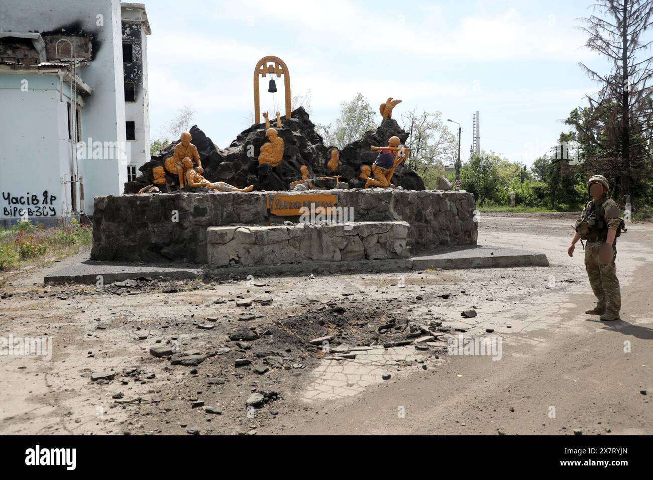 CHASIV YAR, UKRAINE - 18. MAI 2024 - Ein Soldat steht neben dem Denkmal für die Krieger des sowjetisch-afghanischen Krieges vor dem Kulturpalast, der am 23. Juli 2023 durch russische Bombenangriffe zerstört wurde, Chasiv Jar, Donezk, Ostukraine. Stockfoto