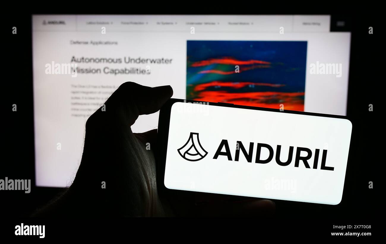 Person, die ein Mobiltelefon mit dem Logo des amerikanischen Verteidigungstechnologie-Unternehmens Anduril Industries Inc. Vor der Webseite hält. Schwerpunkt auf dem Display des Telefons. Stockfoto