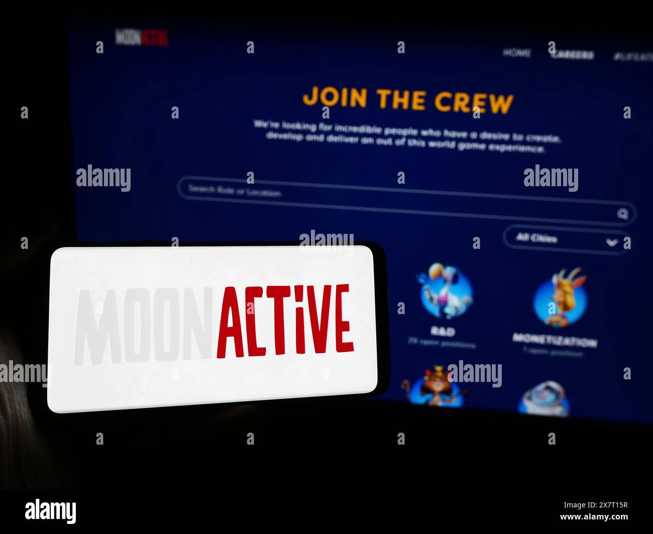 Person mit Smartphone und Logo des israelischen Spieleunternehmens Moon Active Ltd. Vor der Website. Schwerpunkt auf dem Display des Telefons. Stockfoto