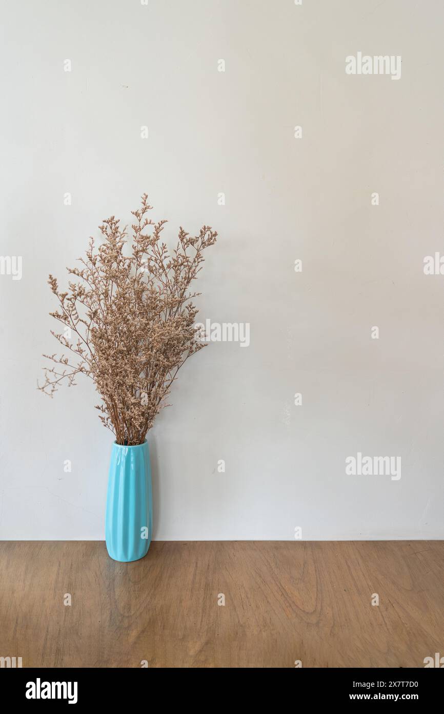 Getrocknete Blume in türkisfarbener Vase auf Holztisch über beigefarbenem Wandhintergrund Stockfoto