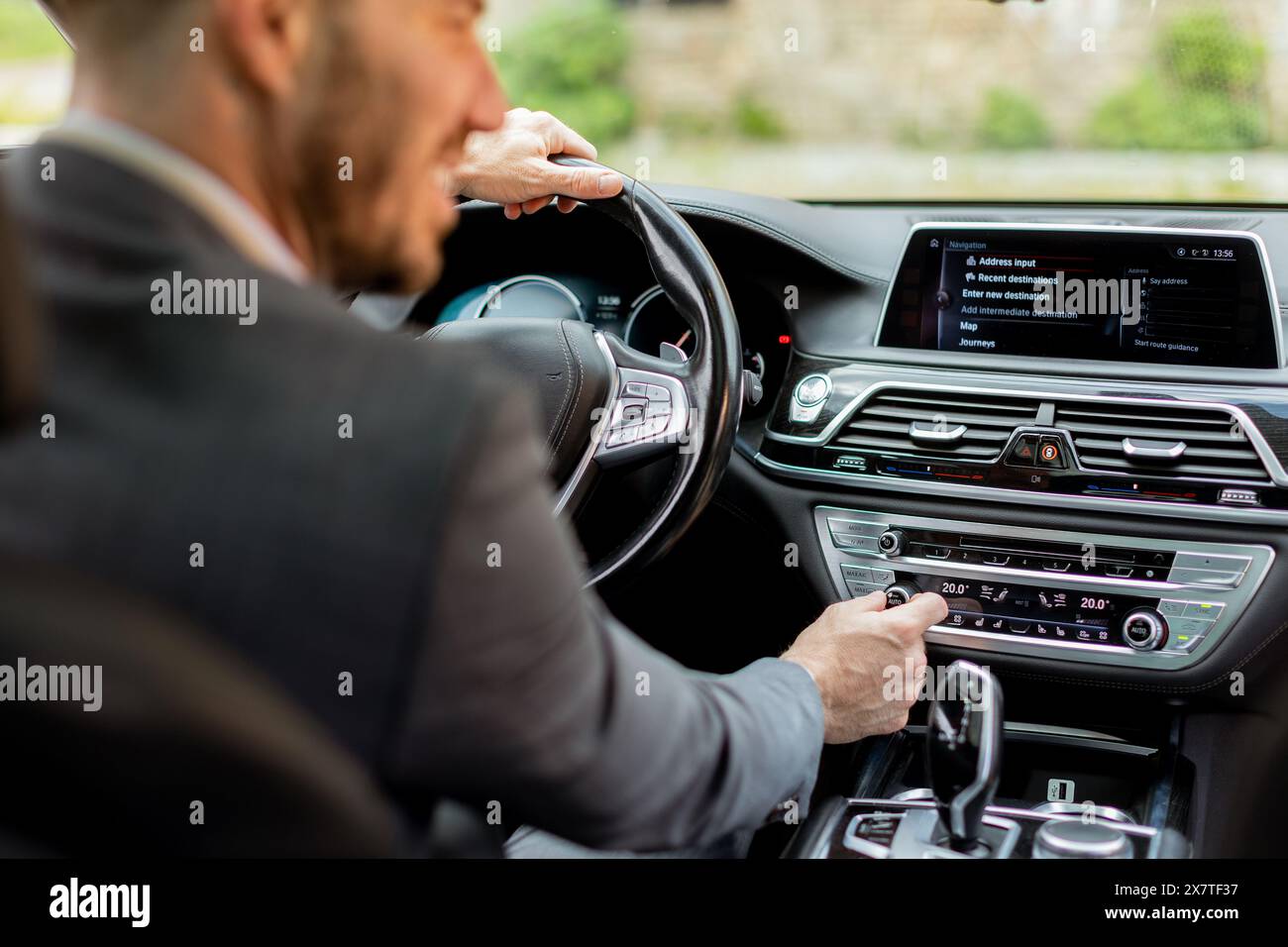 Ein Mann in einem Business-Anzug passt die Klimaanlage während der Fahrt an Stockfoto