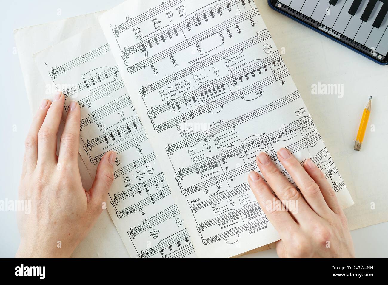 Die Hände einer Person werden auf einem Notenblatt mit Bleistift und Tastatur im Hintergrund angezeigt Stockfoto