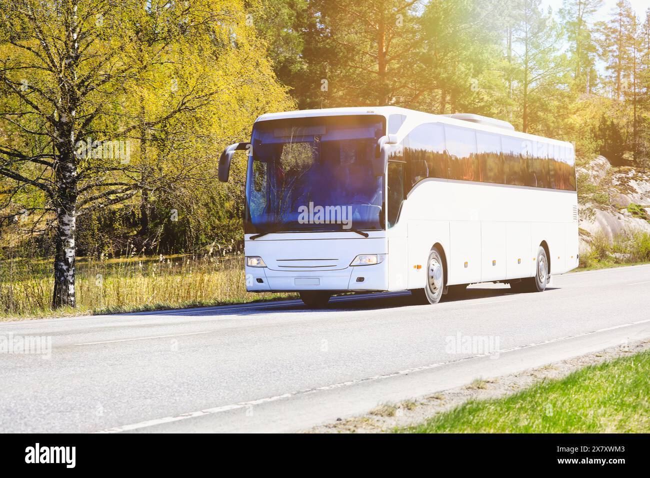 Der weiße Reisebus bringt Passagiere durch die ländliche Landschaft in der warmen Frühlingssonne. Stockfoto