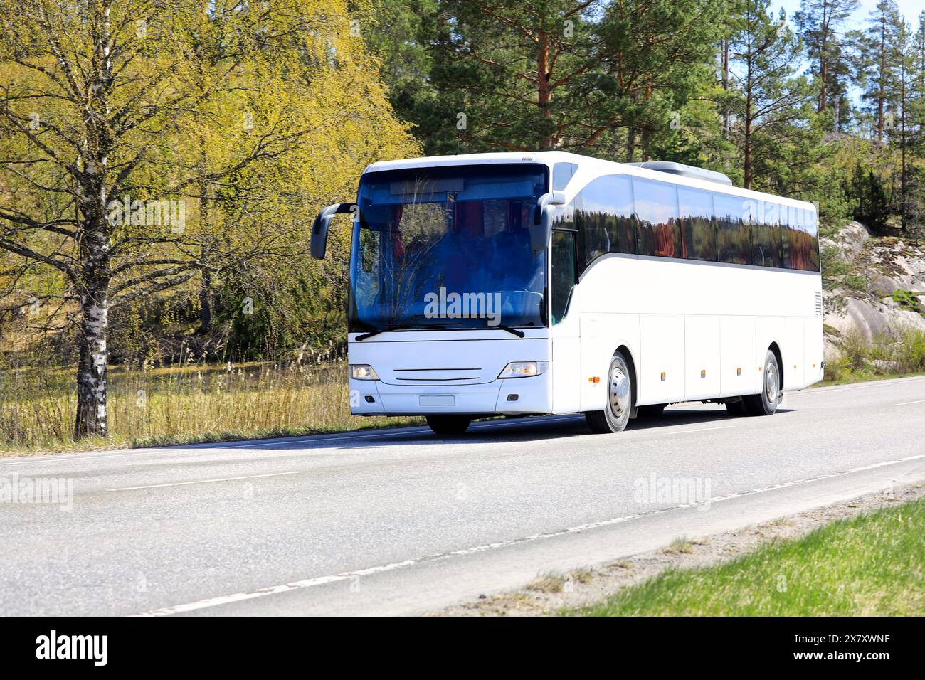 Der weiße Bus bringt Passagiere an einem sonnigen Frühlingstag durch die ländliche Landschaft. Stockfoto