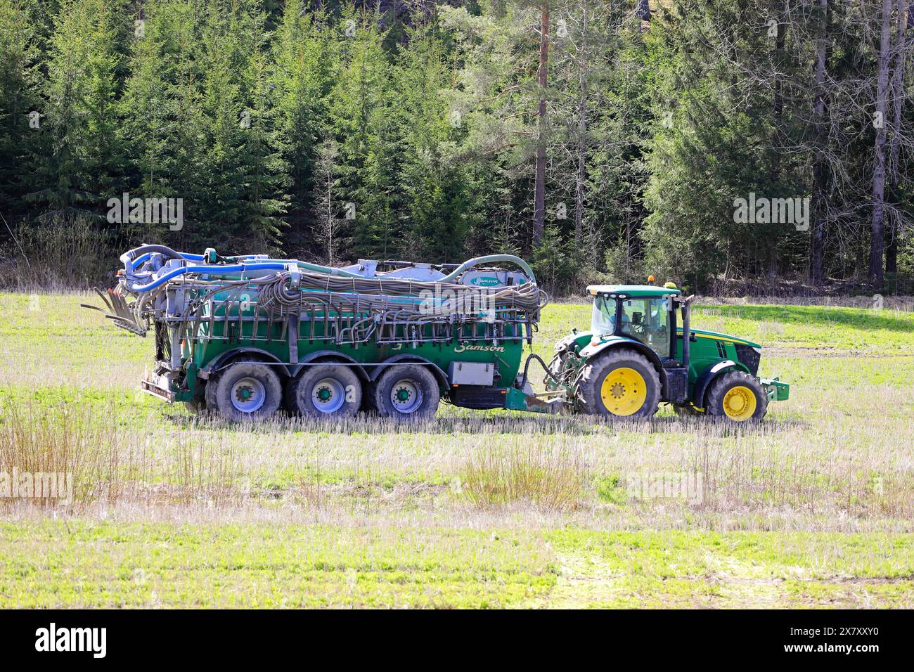 John Deere 7230R-Traktor und Samson PG-Schlammpanker auf Stoppelfeldern zur Injektion von Gülle zur Düngung. Paimio, Finnland. Mai 2024. Stockfoto