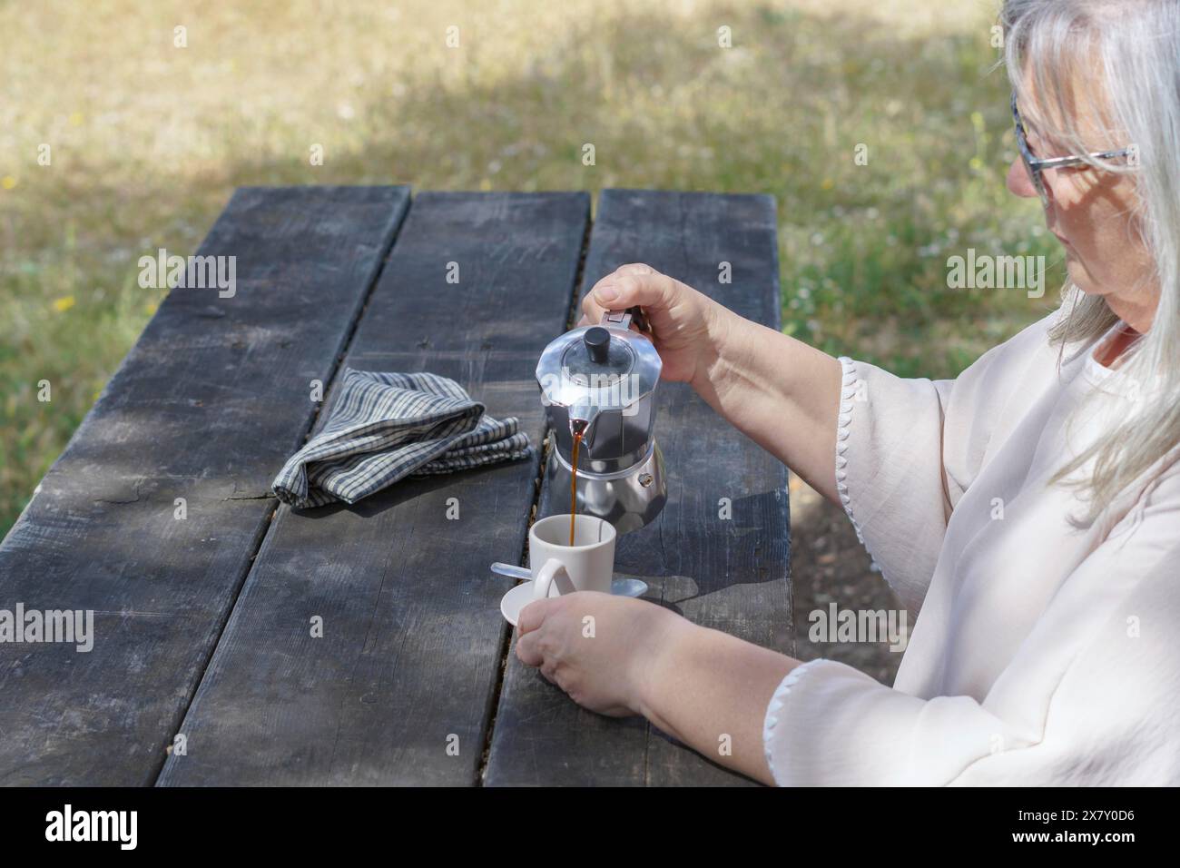 Frau, die im Profil gesehen wurde und sich auf dem Land einen Kaffee auf einem Holztisch servierte Stockfoto