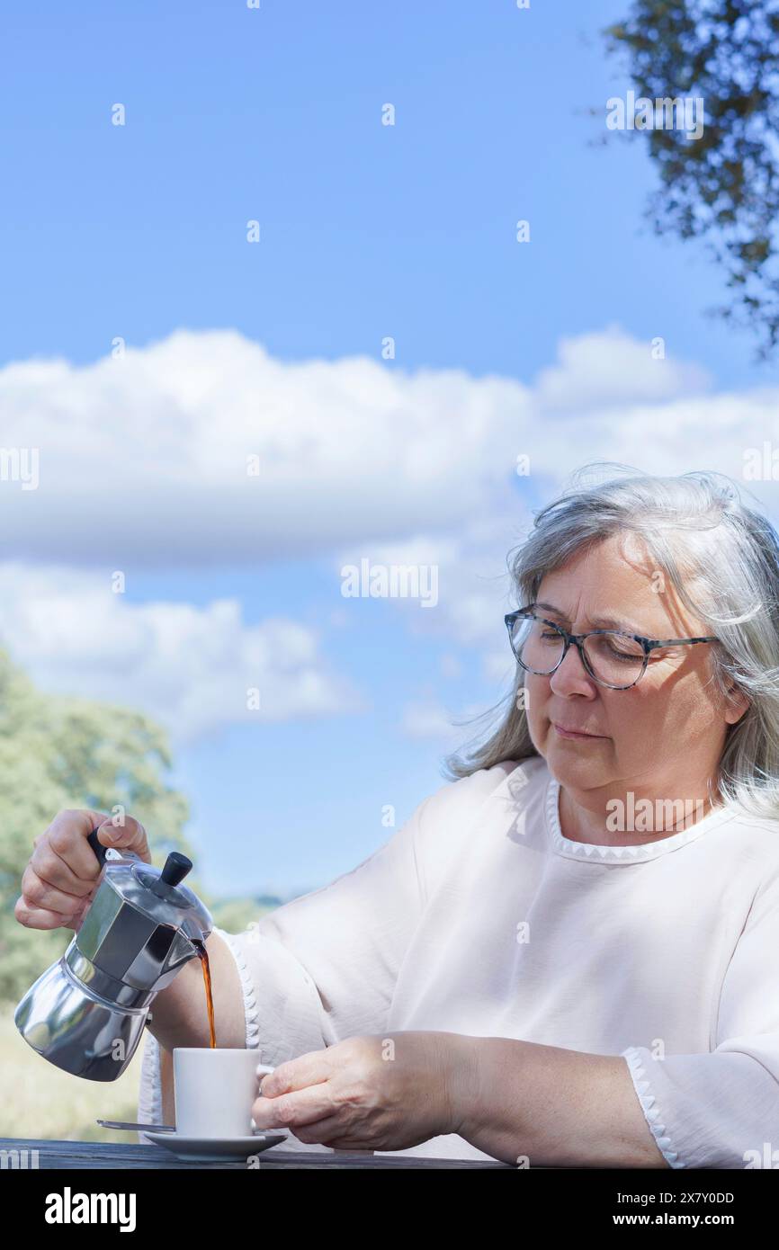 Nahaufnahme einer Frau, die sich an einem Tisch auf einem Feld Kaffee serviert, mit blauem Himmel und Wolken im Hintergrund Stockfoto