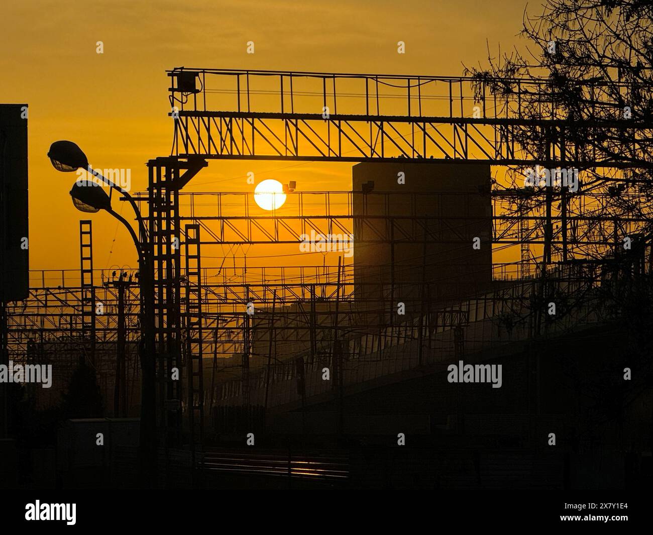 Sonnenuntergang hinter einer Industrieszene mit Stromleitungen und Strukturen, die sich gegen den Himmel schmiegen. Warme, orangene Töne prägen die Szene und schaffen ein Gefühl der Ruhe inmitten der Industrie. Stockfoto