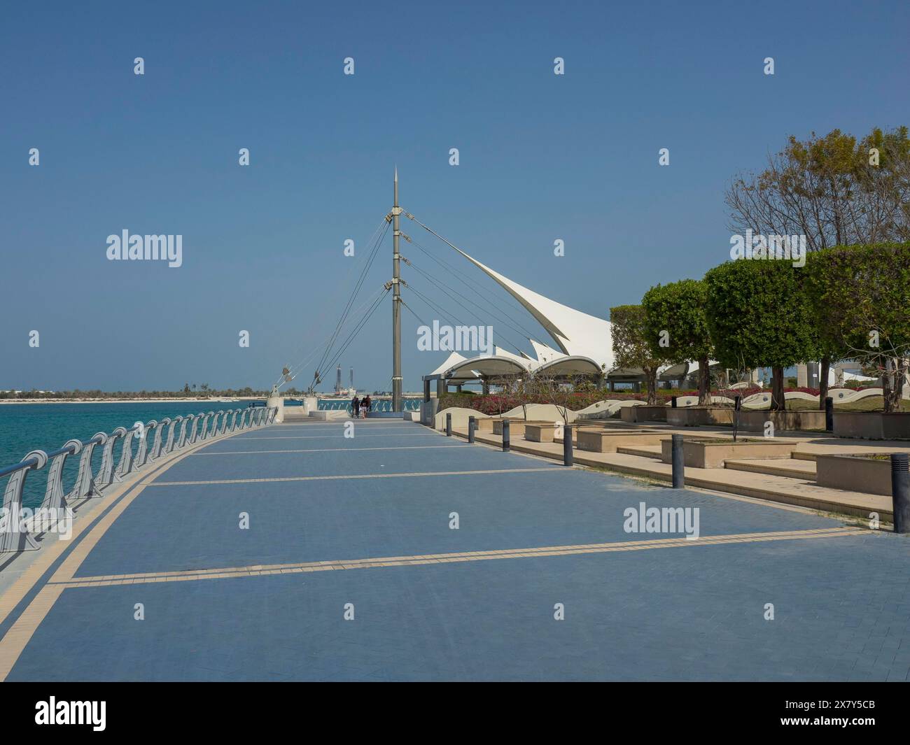 Weißes Zeltdach und Promenade entlang einer Küste, moderne Architektur unter einem klaren blauen Himmel, palmengesäumte Promenade am Meer mit Wolkenkratzern und Lant Stockfoto