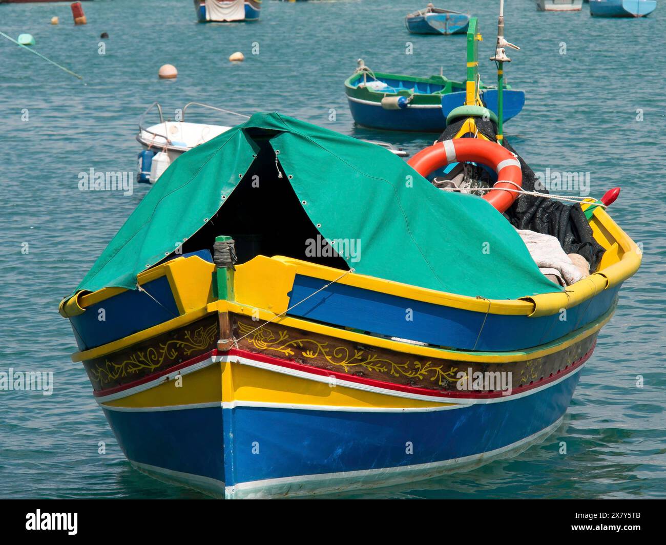 Ein farbenfrohes Fischerboot mit grünem Stoffbezug und Rettungsschirm vor Anker, viele farbenfrohe Fischerboote in einem Hafen im Mittelmeer, Marsaxlokk, m Stockfoto