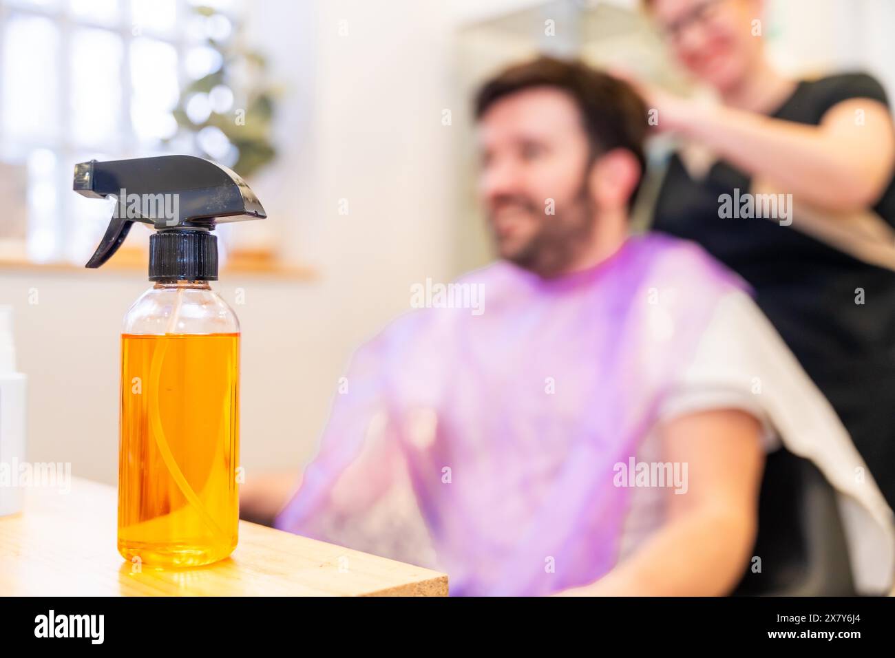 Flasche mit Wasser, um die Haare der Kunden im Salon mit einem Mann mit Flügel im Hintergrund zu besprühen Stockfoto