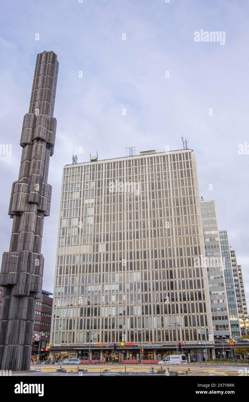 Ein modernes Hochhaus mit einer Glasfassade und einer auffälligen Skulptur im Vordergrund, grauem Himmel und urbaner Umgebung. Stockholm, Schweden, E Stockfoto