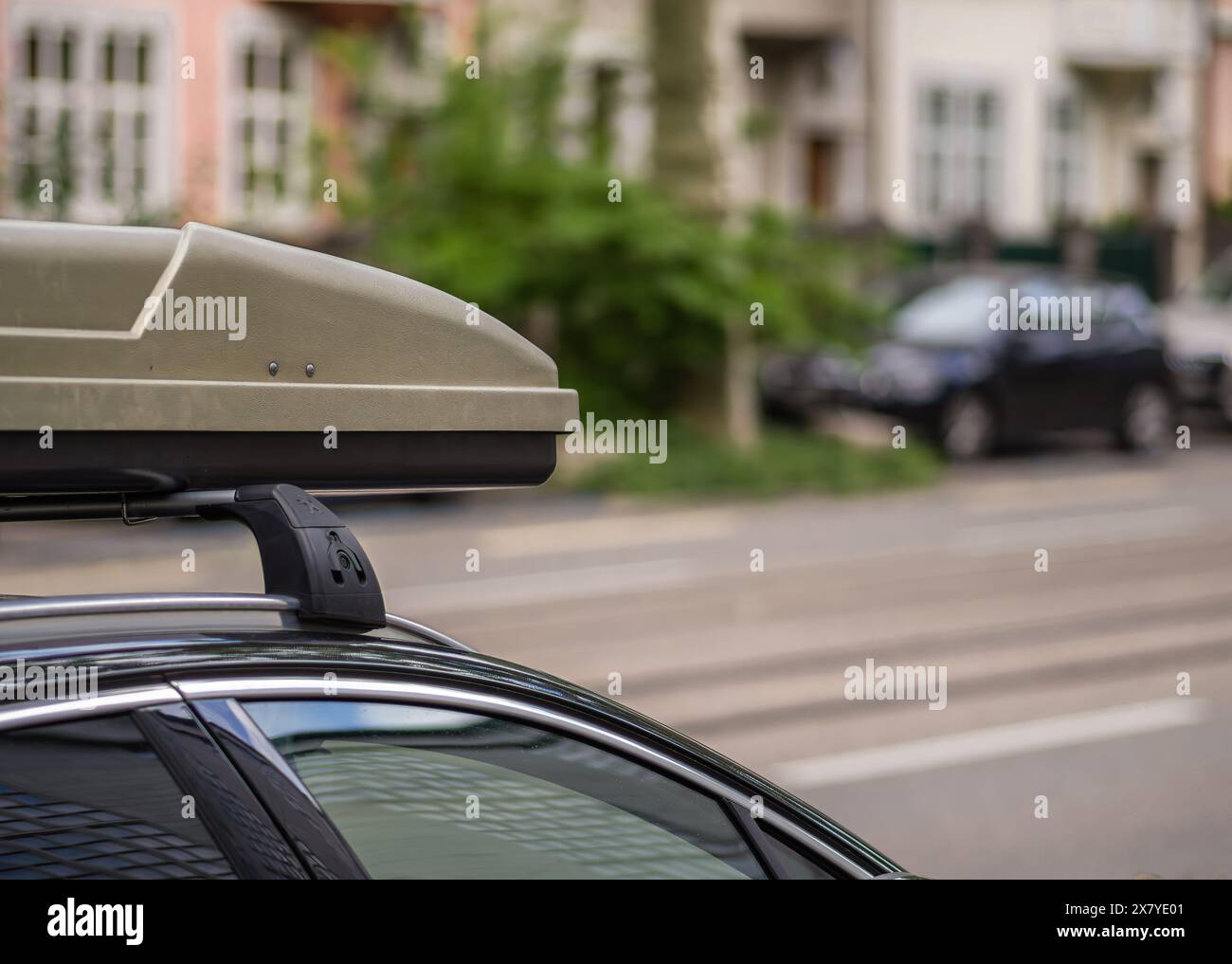 Nahaufnahme eines Autos mit beigefarbenem Dachkasten auf Dachträger, der auf einer städtischen Straße mit verschwommenem Hintergrund geparkt ist Stockfoto
