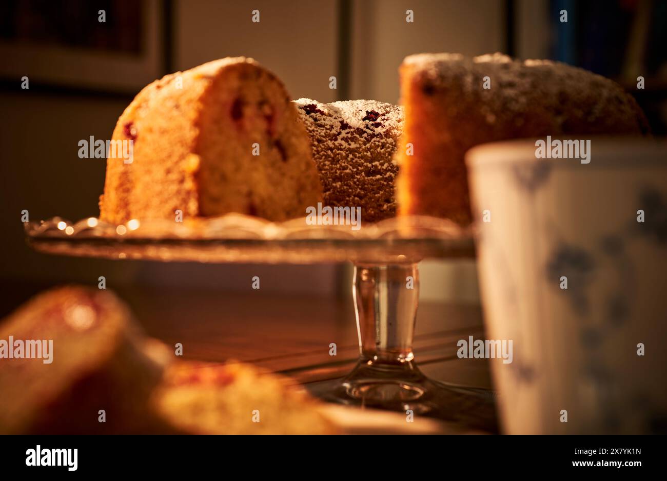 Donut auf einem glasierten Teller. Innendetail mit Doughnut- oder ringförmigen Cake-Ciambella auf Glasständer mit einer Tasse heißem Kaffee und einer Bibliothek. Hygge-Konzept Stockfoto