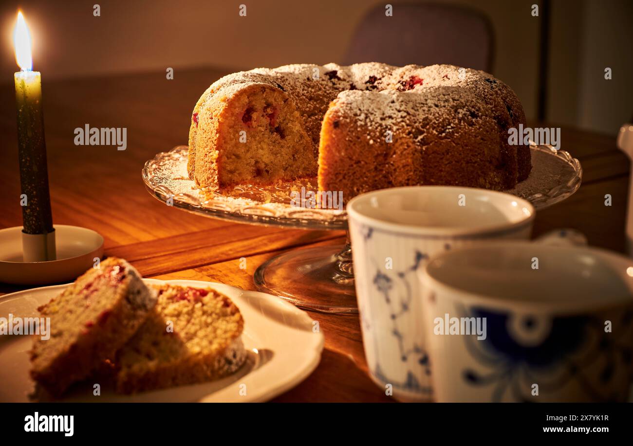 Romantisches Ambiente mit Donut, heißem Kaffee und brennender Kerze. Gemütliche Einrichtung auf Holztisch mit einem Donut und einer Tasse warmen Tee unter Kerzenlicht Stockfoto