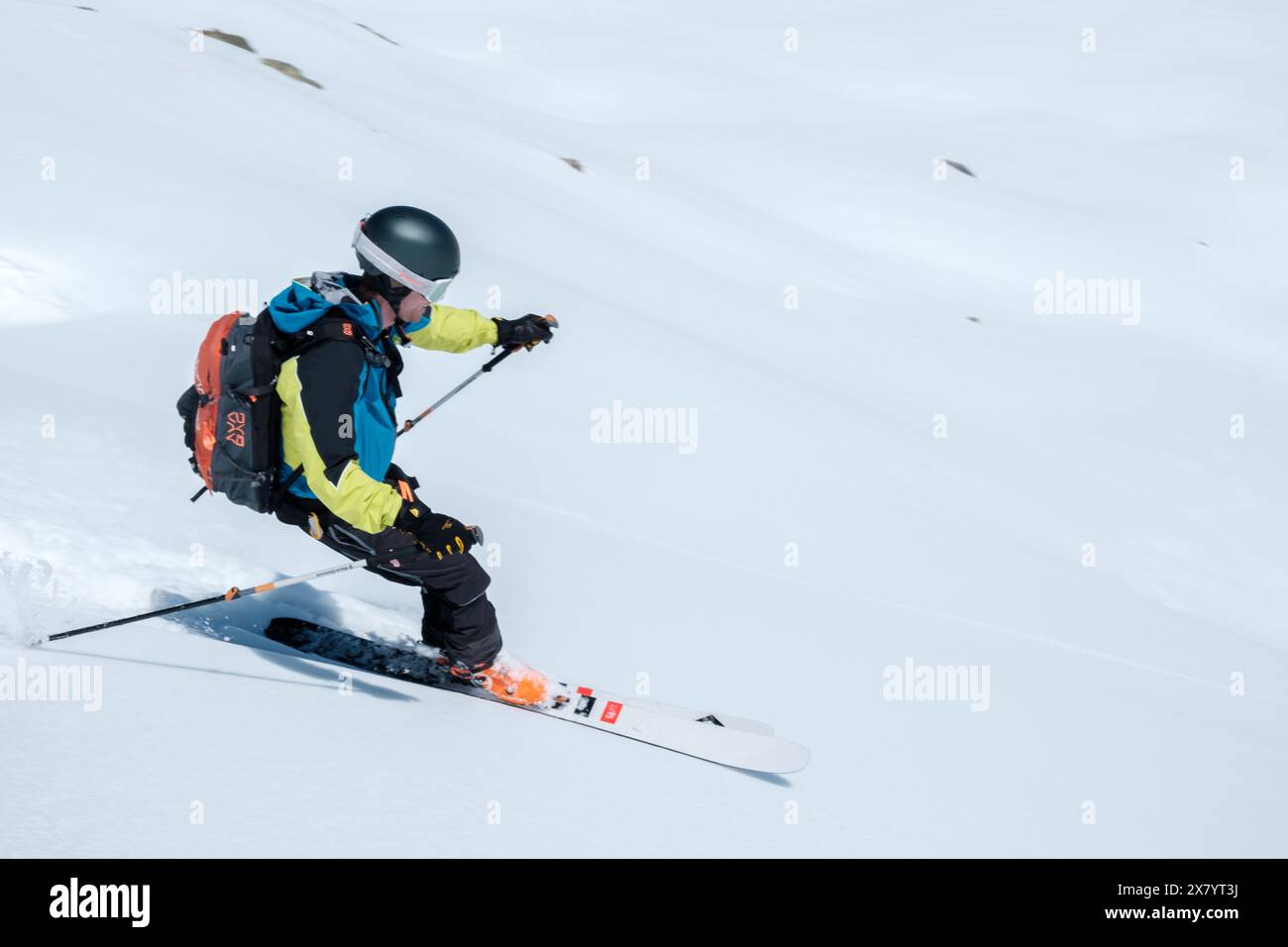 Skibergsteiger mit Helm und Rucksack, der im Neuschnee bergab geht Stockfoto