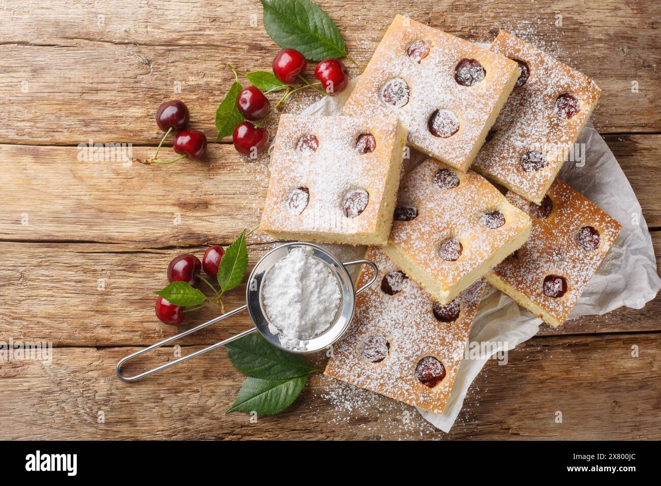 Bublanina tschechischer und slowakischer Kirsch-Bubble-Kuchen mit Puderzucker-Nahaufnahme auf dem Pergament auf dem Holztisch. Horizontale Draufsicht Stockfoto