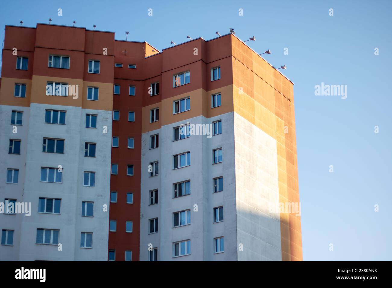 Vor dem Hintergrund eines blauen Himmels steht ein hoch aufragendes Gebäude mit urbanem Design und Verbundwerkstoff. Die Fassade der Wohnung spiegelt das A wider Stockfoto