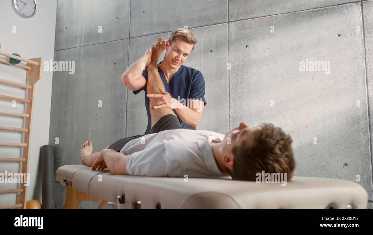 Professioneller Sportphysiotherapeut, der mit jungen männlichen Athleten an Muskelgruppen oder Gelenken arbeitet. Sportler erholt sich von einer Verletzung. Traumaprävention Therapie oder Rehabilitation. Gesundheitskonzept. Stockfoto