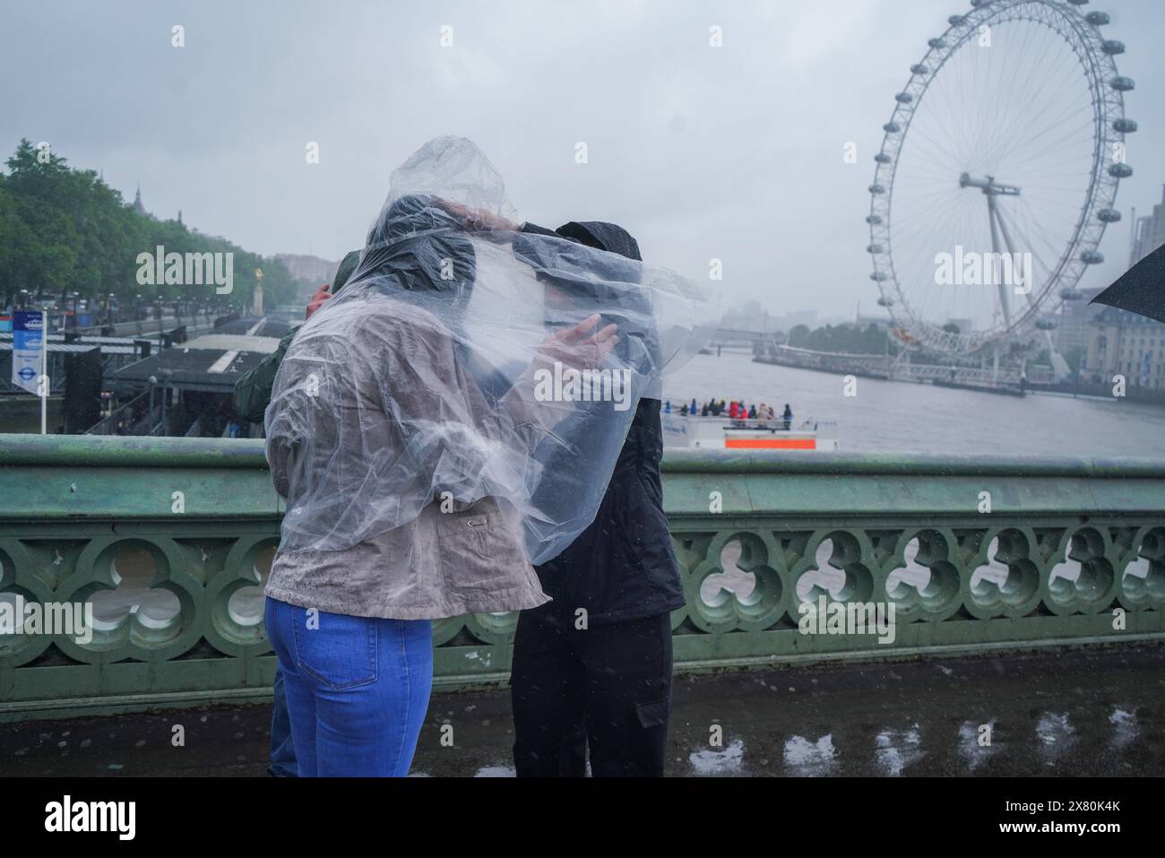 Westminster, London, Großbritannien. Mai 2024. Einem Fußgänger wird dabei geholfen, einen Regenponcho auf der Westminster Bridge anzuziehen und den starken Regenschauern zu trotzen. Eine Wetterwarnung wurde für Überschwemmungen und Gewitter in London und Südengland veröffentlicht Credit: amer ghazzal/Alamy Live News Stockfoto