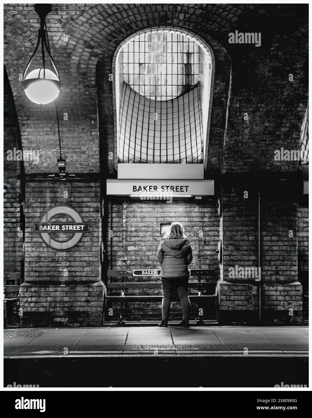 Schwarzweißbild - eine Person steht auf dem Bahnsteig der Baker Street, gegenüber der Position der Kamera und wird von oben beleuchtet Stockfoto
