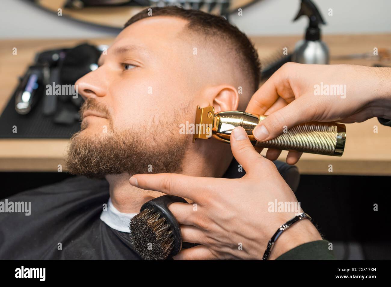 Der Friseur schneidet den Bart des jungen Mannes mit dem Trimmer in der Nähe des Friseurs in Form. Der Friseur serviert männliche Gäste im Friseursalon Stockfoto