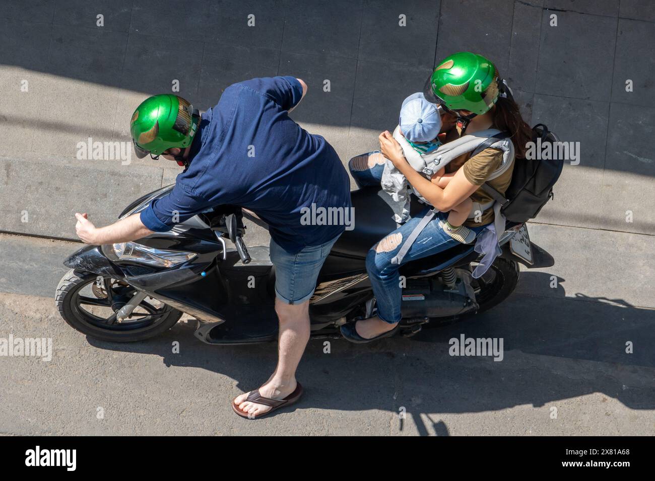 Der Fahrer überprüft die Leuchte am Motorrad, auf der eine Frau mit einem kleinen Kind sitzt Stockfoto