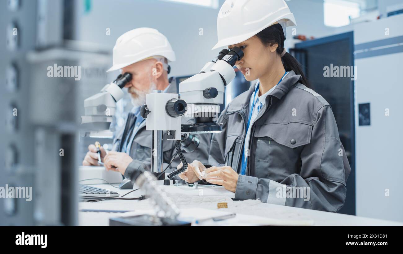 Electronic Manufacturing Factory: Zwei Ingenieure untersuchen kleine Teile von Industrieanlagen mit einem Mikroskop. Techniker testen neue Werkskomponenten auf Produktionsqualität. Stockfoto