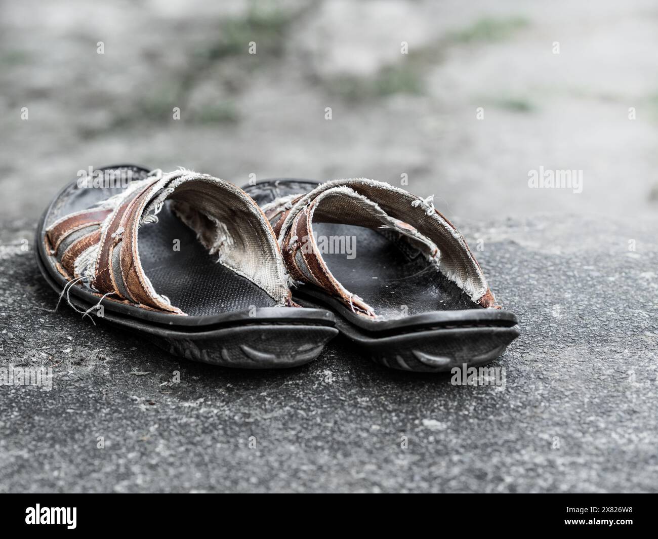 Ein Paar abgenutzte Sandalen, die auf rauer Betonoberfläche ruhen und die Not und Reise symbolisieren. Der Hintergrund ist unscharf. Stockfoto