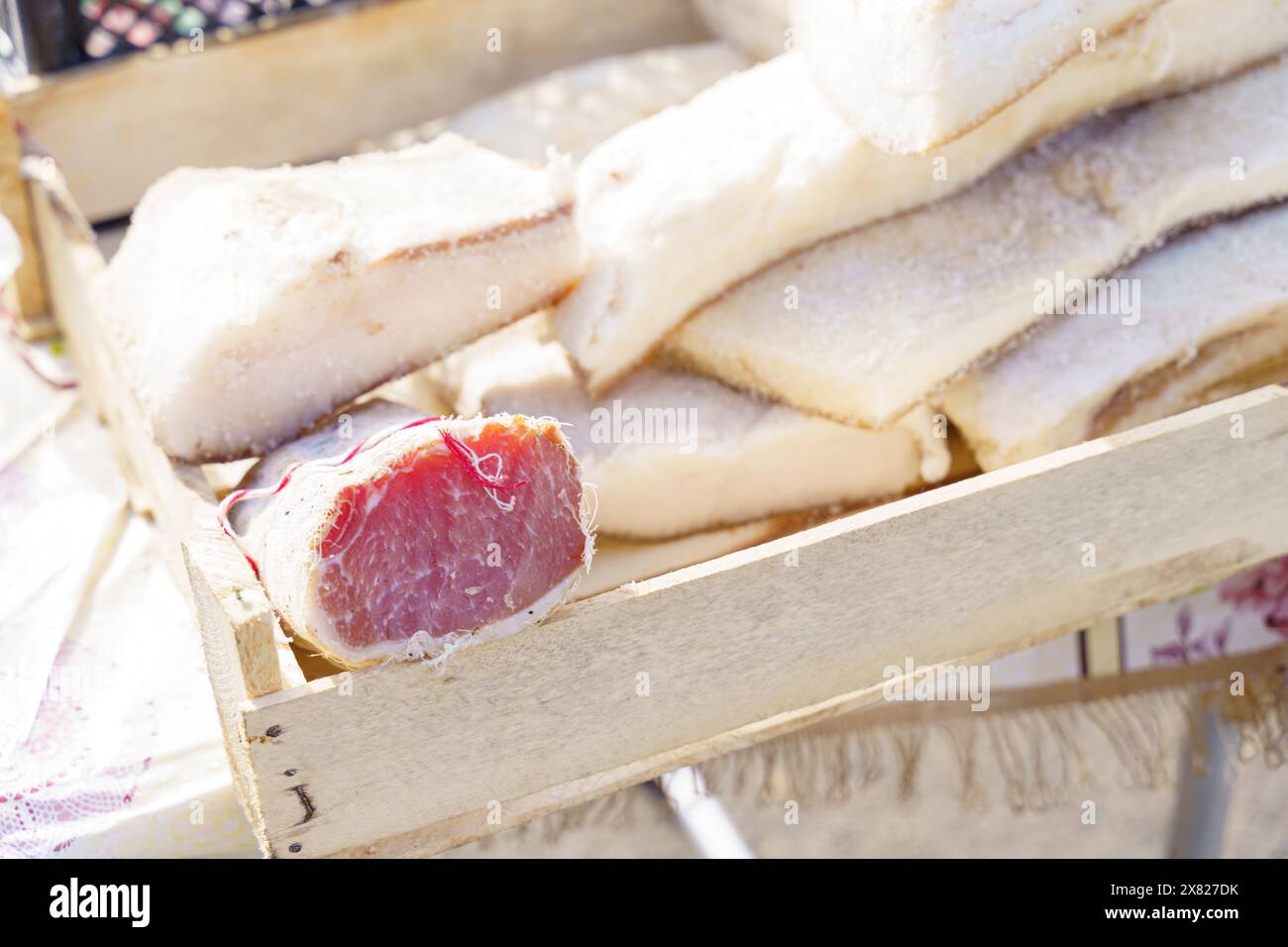 Verschiedene hausgemachte Schweinefleischprodukte, darunter Schmalz, Balyk und Polendvitsa, werden auf einem rustikalen Holztablett auf einem Markt im Freien ausgestellt. Die Produkte sind s Stockfoto